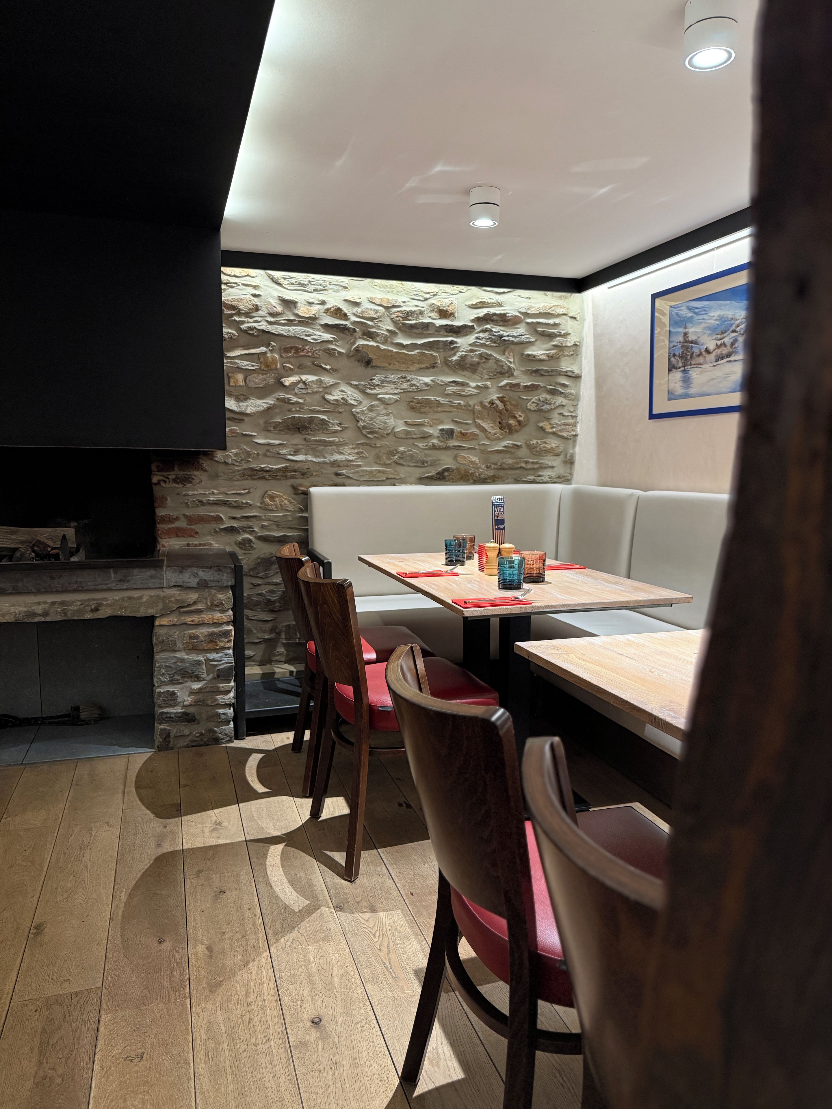 Un comedor con pared de piedra, suelo de madera y una mesa dispuesta con servilletas rojas y vasos.