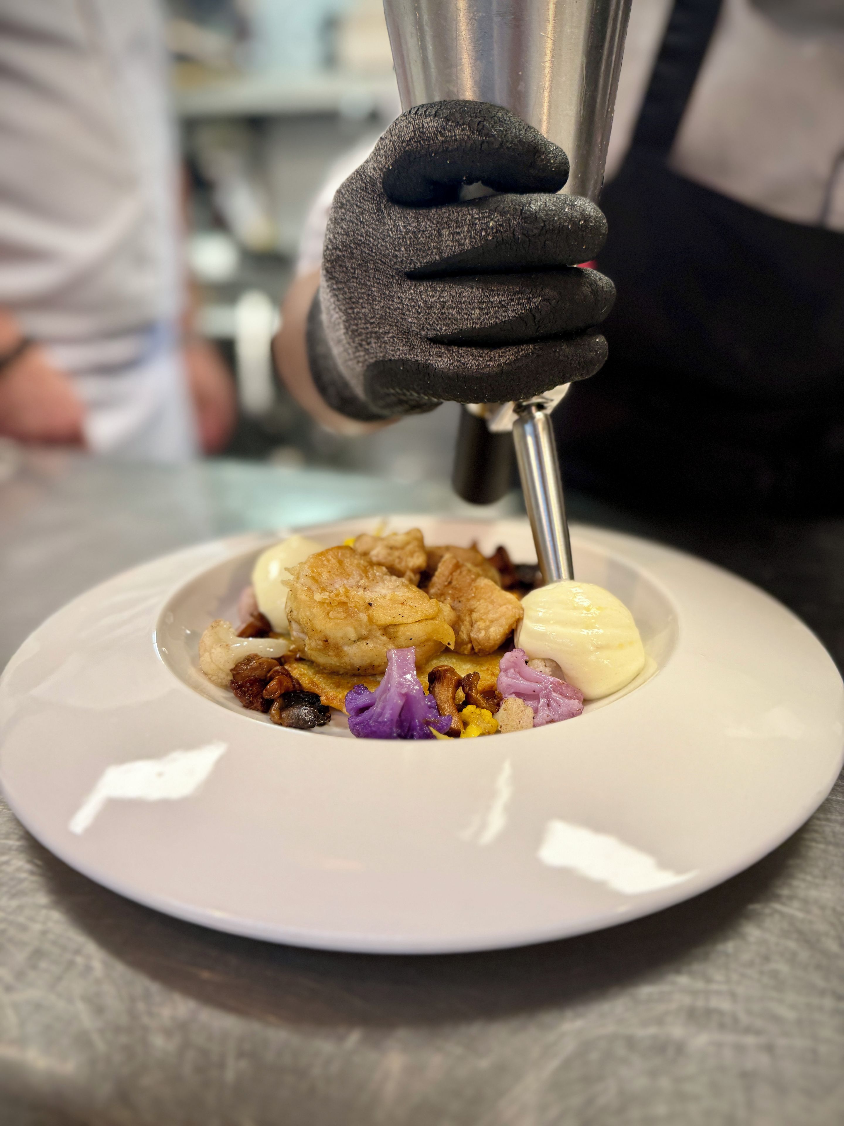 A person wearing a black glove using a metal tool on a plate with food.