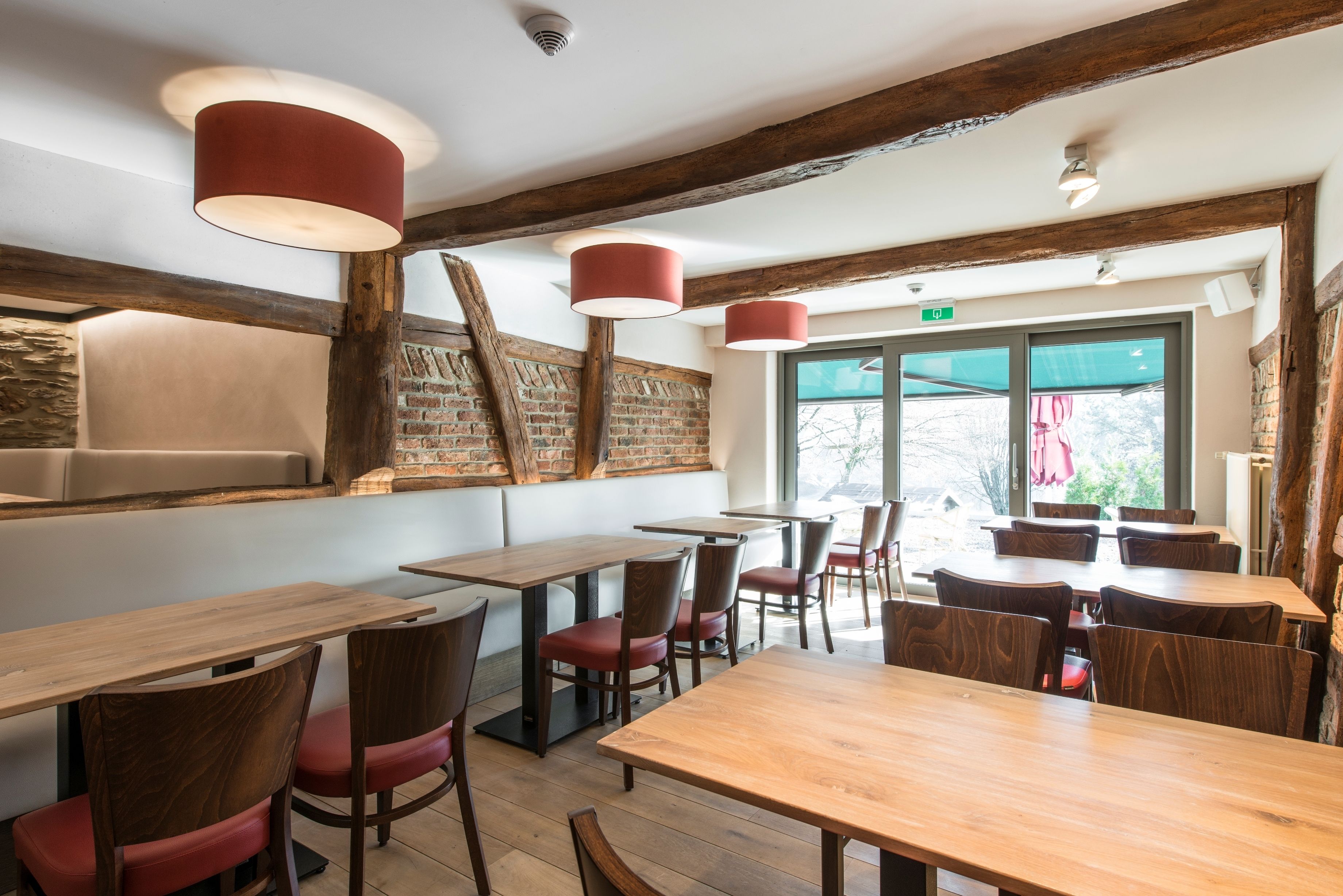 Interior de restaurante con mesas y sillas de madera, paredes de ladrillo visto e iluminación colgante.
