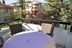 A balcony with wicker chairs and a table, overlooking a residential area with trees and buildings. - Ankara Hotel Pino (Ankara)