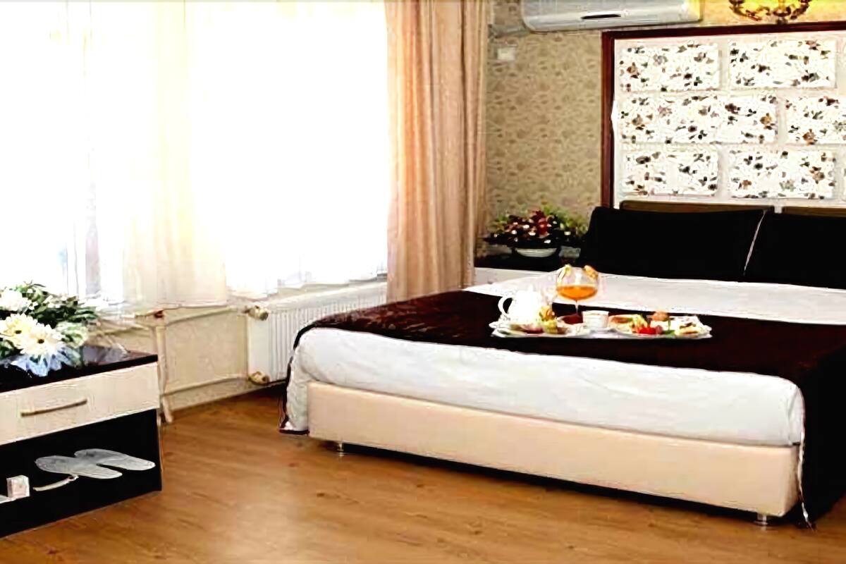 A neatly made bed with a tray of breakfast items, a bedside table with a vase of flowers, and a window with curtains.