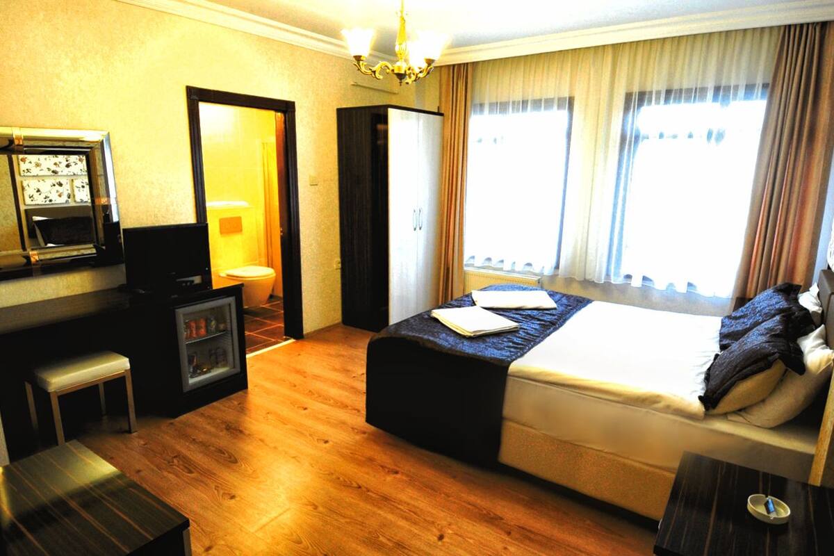 A hotel room with a bed, bedside table, desk with a computer, and a small seating area.