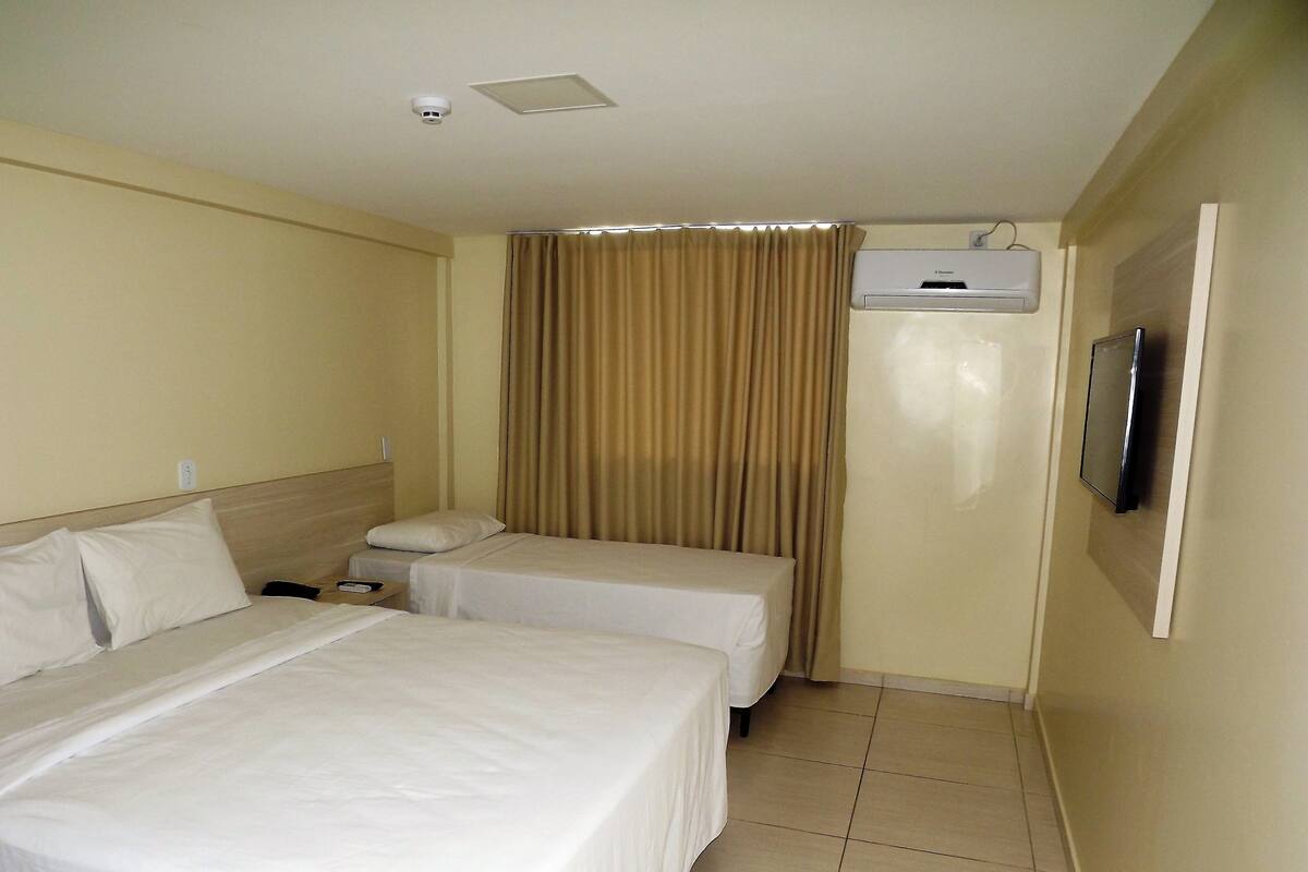 Habitación de hotel con dos camas, televisor, aire acondicionado y una cámara de seguridad.