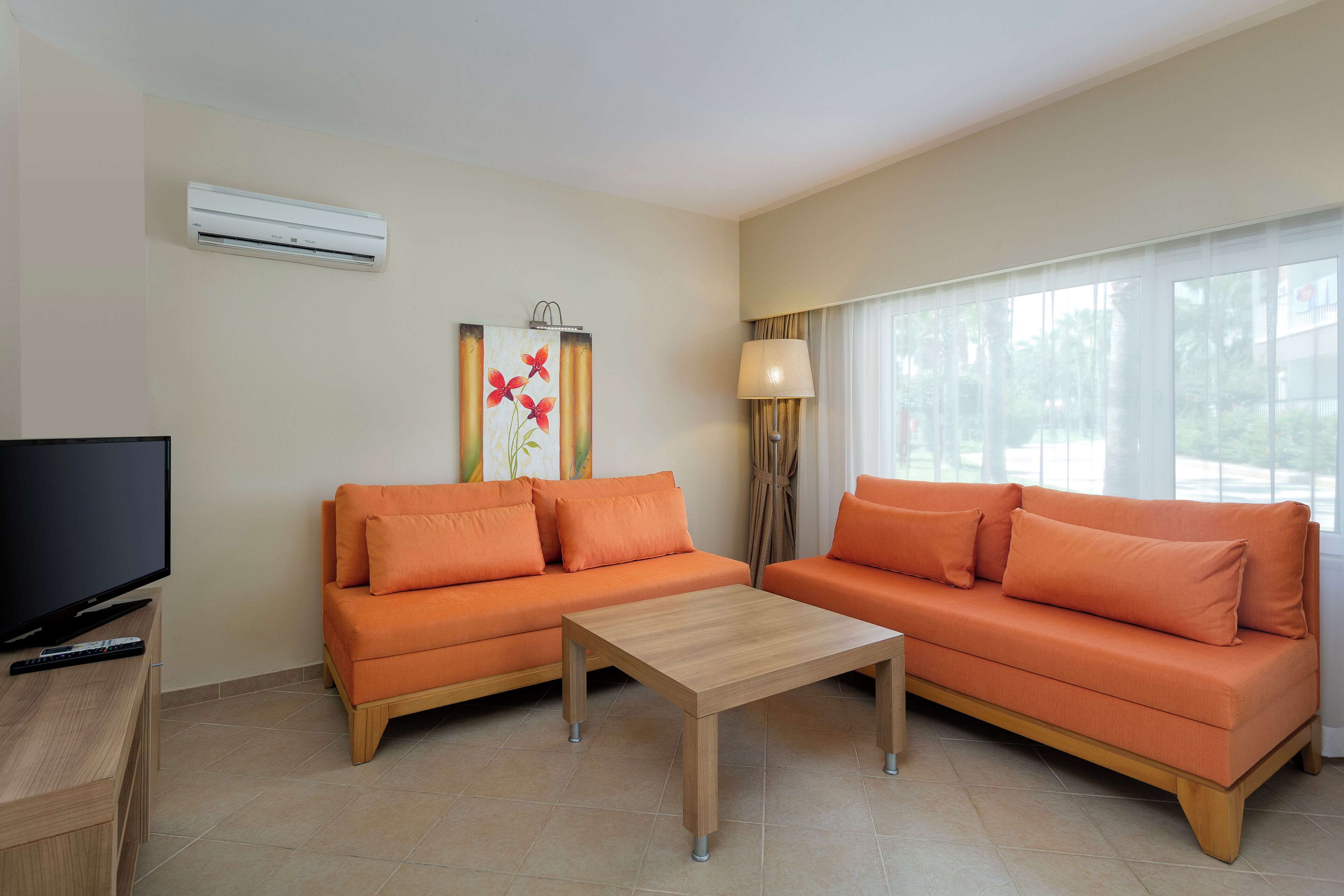 A modern living room with two orange sofas, a wooden coffee table, a flat-screen TV, and a painting on the wall.