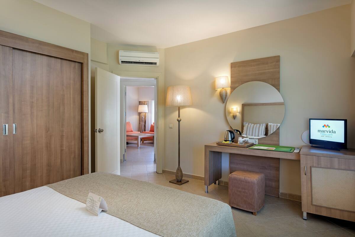 A hotel room with a bed, a desk, a chair, a lamp, a mirror, and a television.