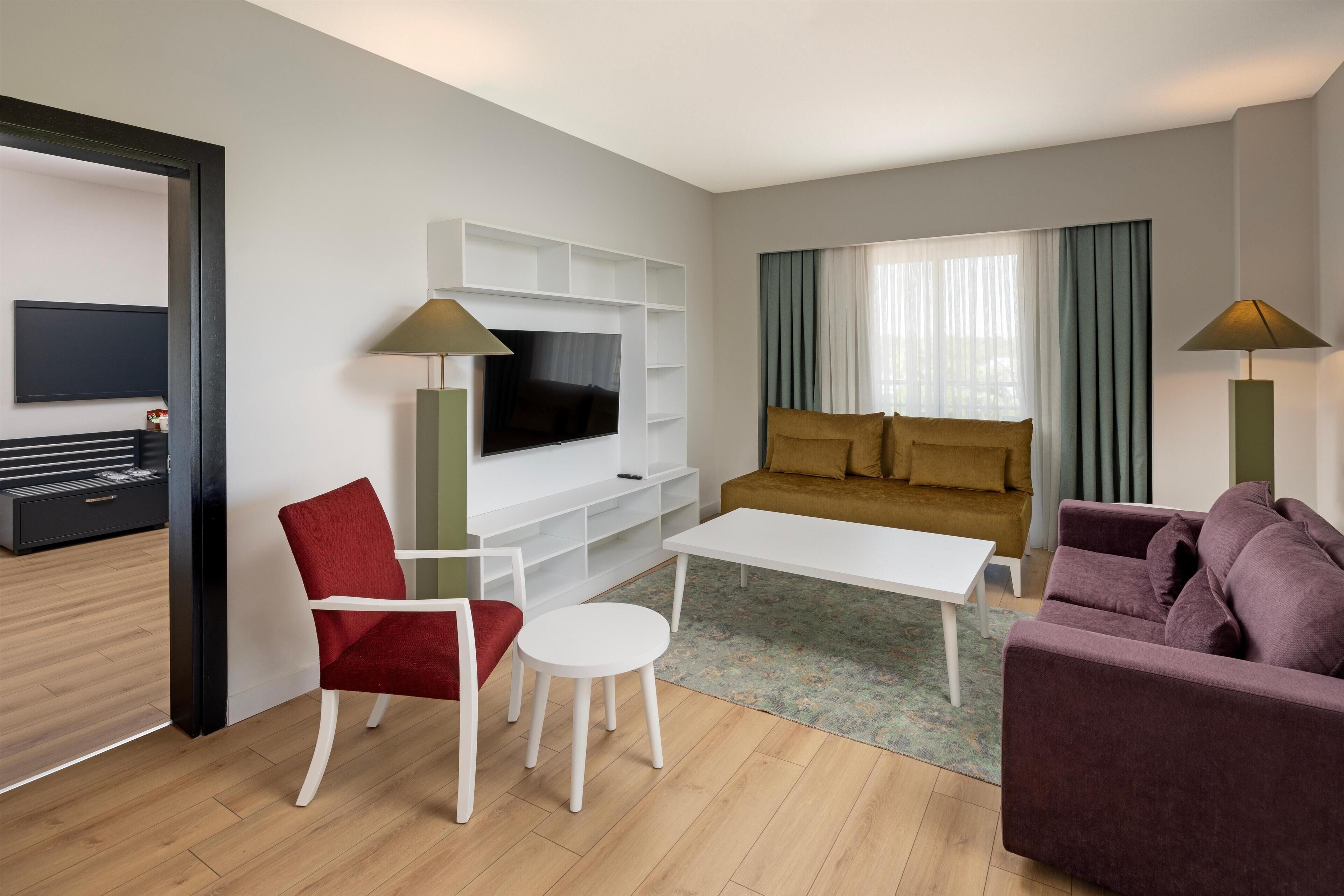 A modern living room with a flat-screen TV, a sofa, a red chair, a white coffee table, and two floor lamps.