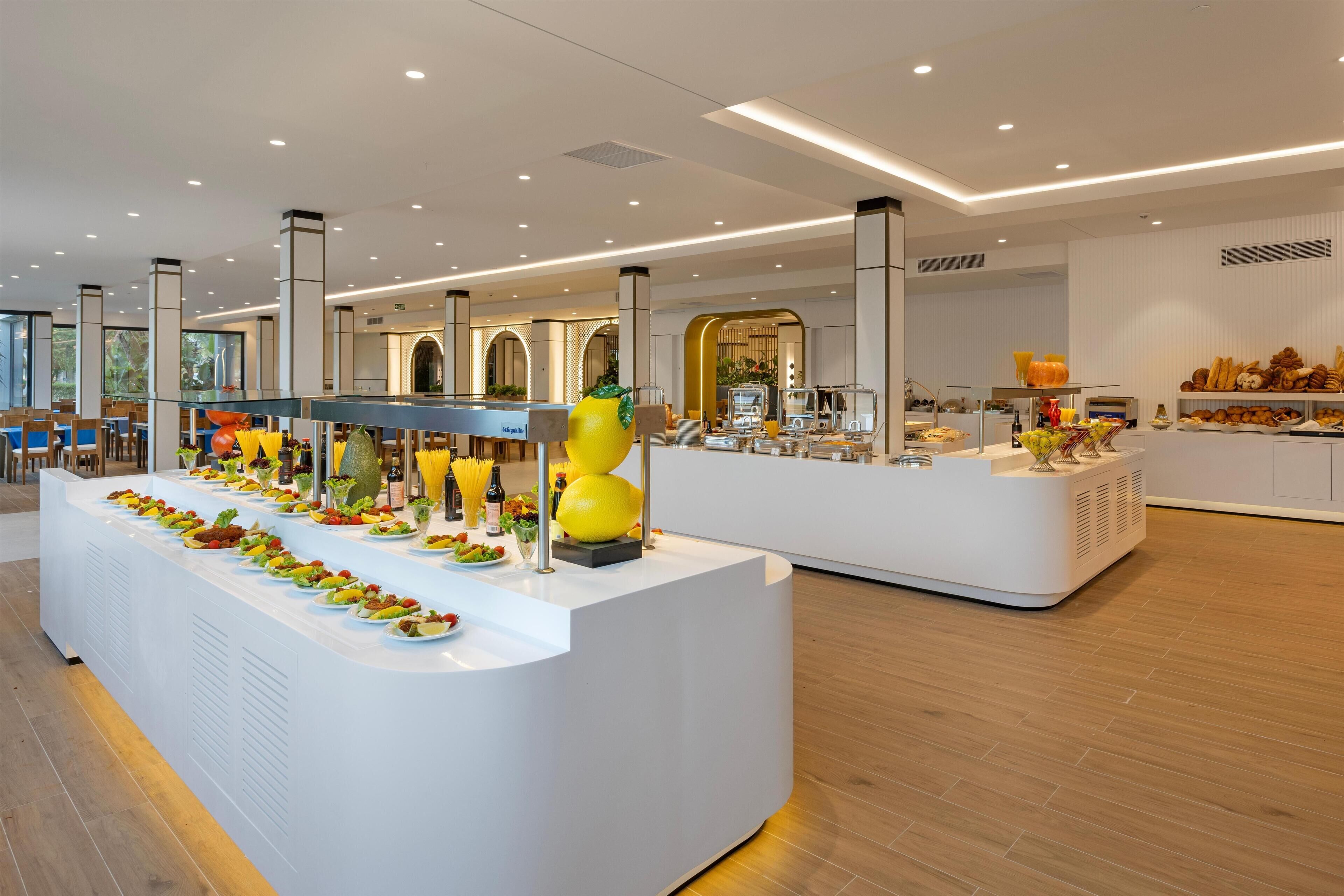 A modern hotel lobby with a buffet area featuring various food stations and a seating area with wooden tables.