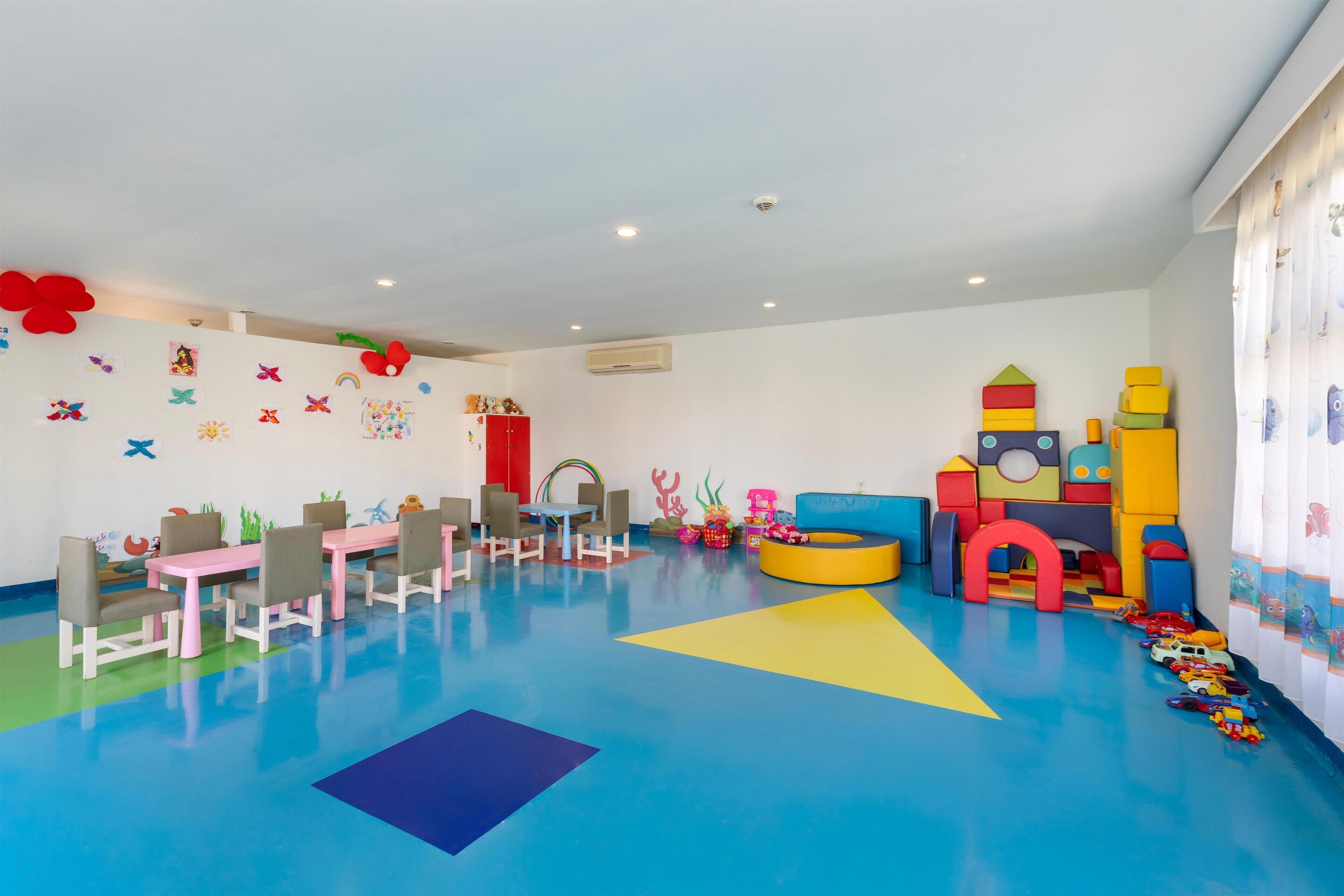 A children's playroom with colorful play mats, a play table, chairs, and various play structures.