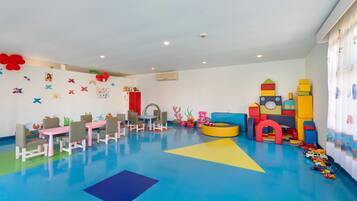 A children's playroom with colorful play mats, a play table, chairs, and various play structures.