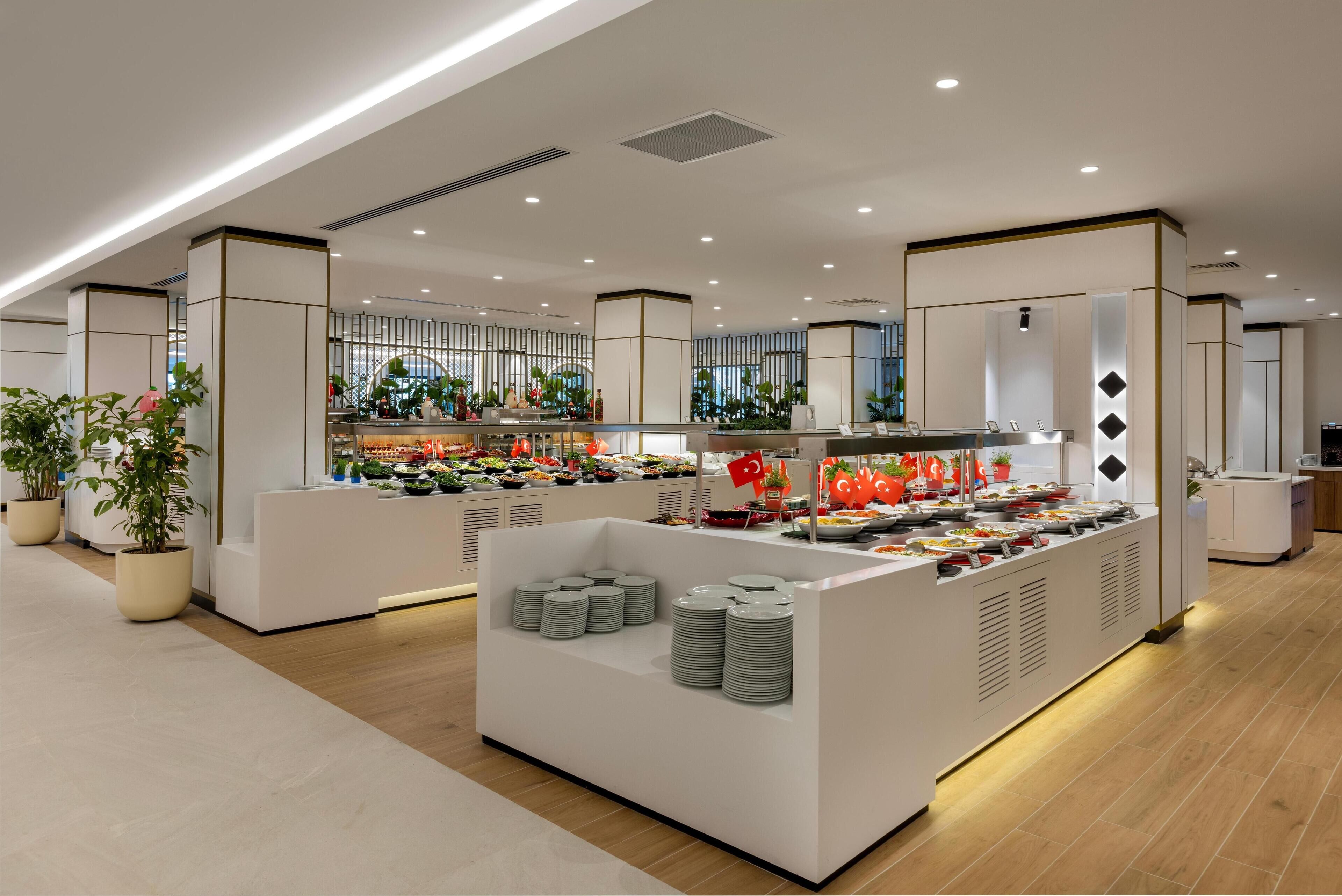 A modern hotel lobby with a central buffet area, potted plants, and a clean, minimalist design.