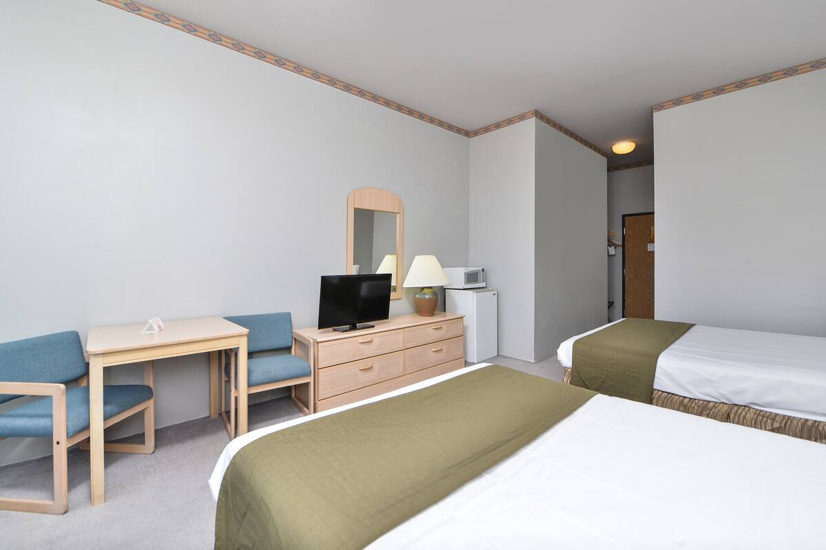 A hotel room with a desk, two single beds, a television, a lamp, and a small refrigerator.