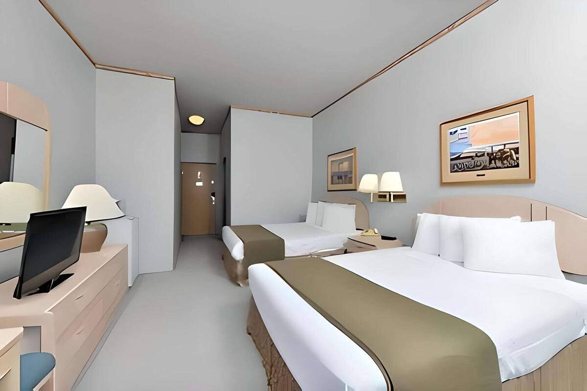 A hotel room with two beds, a desk with a computer, a TV, and a framed picture on the wall.