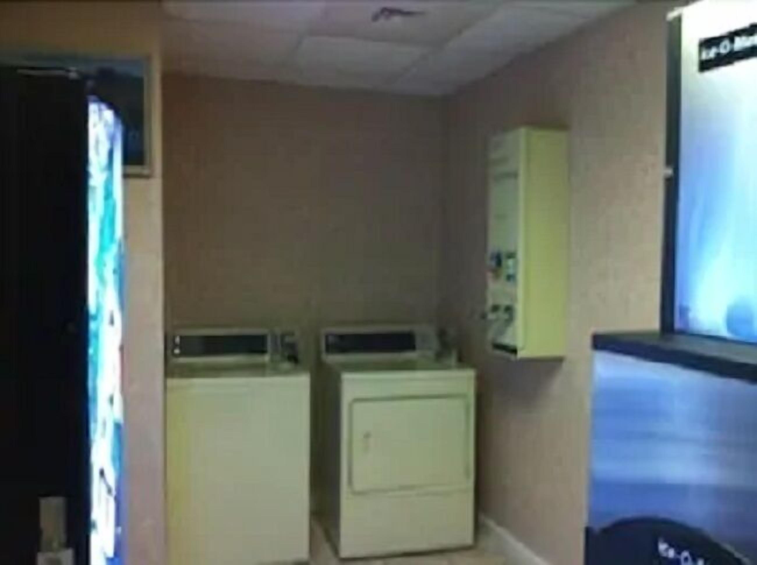 A laundry room with two washing machines and a dryer, a small cabinet, and a television screen.