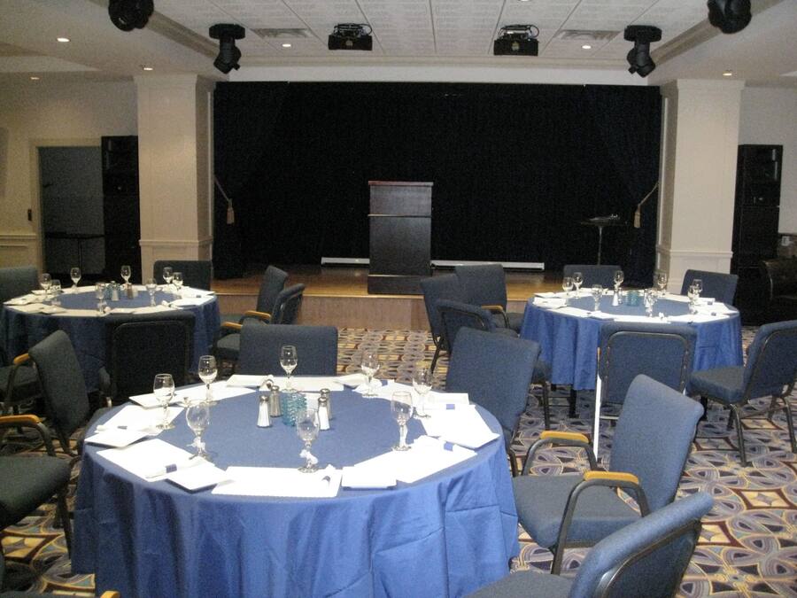 A conference room with round tables, chairs, and a stage with a podium.