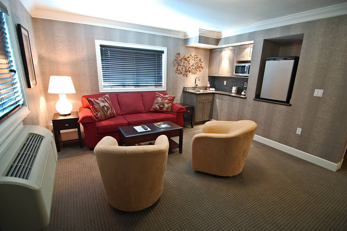 A living room with a red sofa, two armchairs, a coffee table, a lamp, and a wall-mounted fireplace.