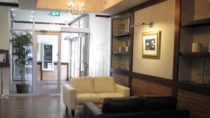A lobby with a beige sofa, a dark sofa, wooden paneling, a chandelier, and a framed picture on the wall. - Billy Barker Casino Hotel (Quesnel)