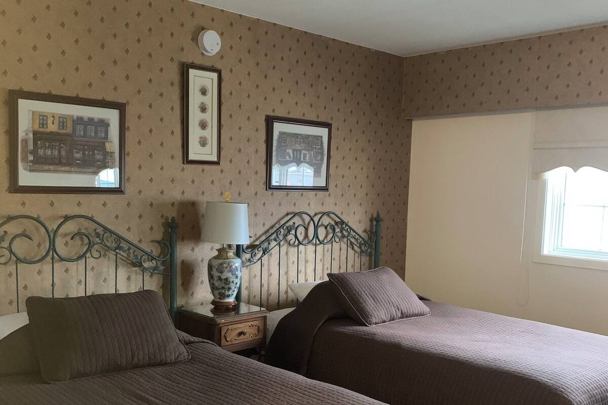 A room with two beds, a nightstand with a lamp, and framed pictures on the wall.