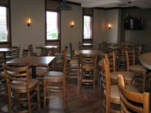 A restaurant interior with multiple wooden tables and chairs, pendant lighting, and windows with views of the outside.
