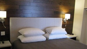 A neatly made bed with white pillows and a dark brown bedspread, positioned between two nightstands with wall-mounted lamps. - Billy Barker Casino Hotel (Quesnel)