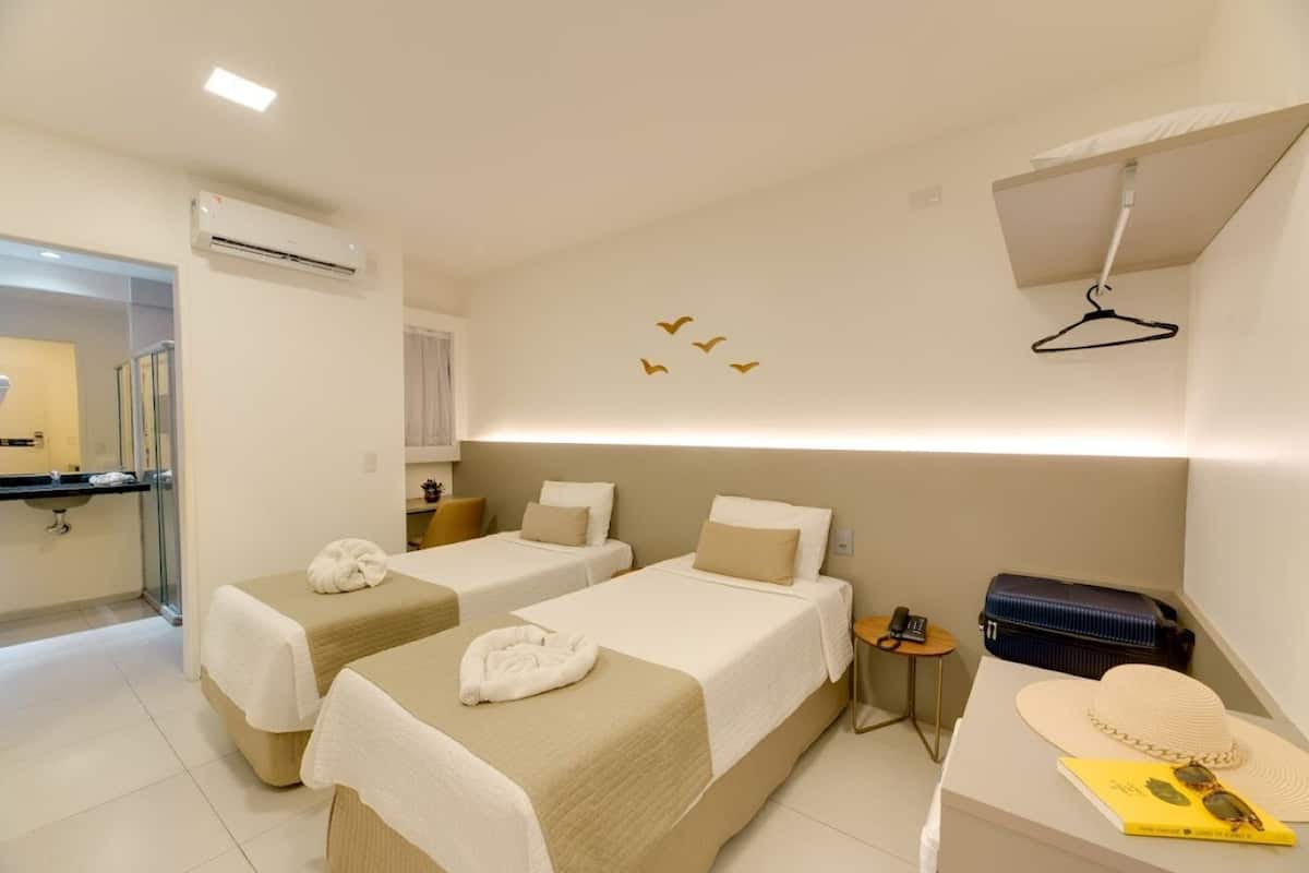 A hotel room with two beds, a small desk, a mirror, and an air conditioning unit.