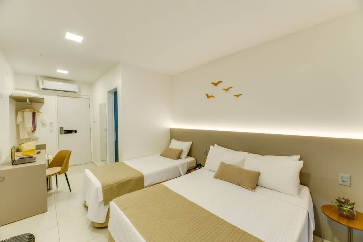 A hotel room with two beds, a desk, a chair, and a small table with a plant.