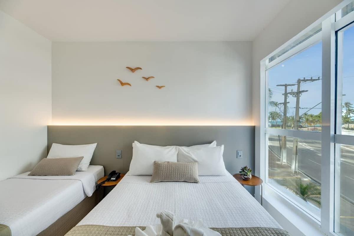 A modern hotel room with two beds, a large window, and a view of the street.
