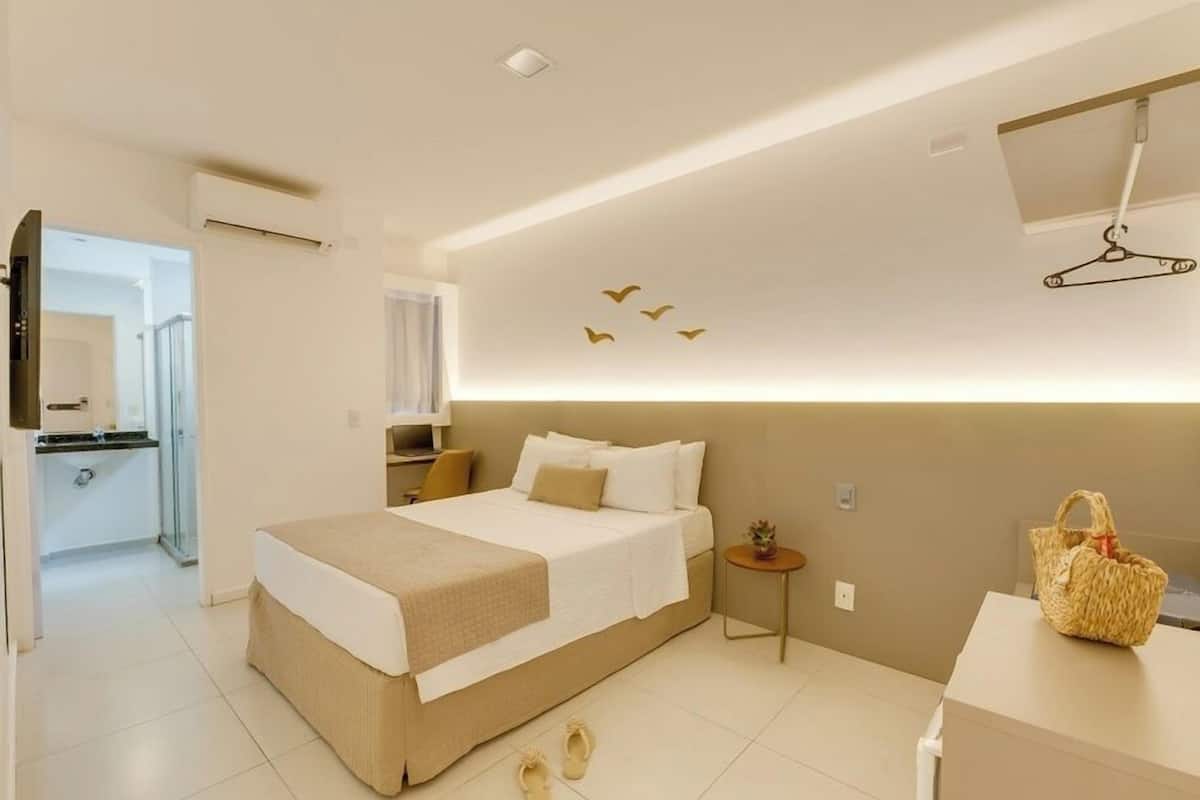 A modern hotel room with a large bed, a small bedside table, a TV, and a hanging coat rack.