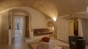 A cozy room with a stone ceiling, a sofa, a small table, and a chair. - Fra i Sassi - Residence (Matera)