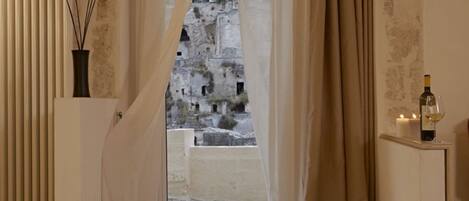A room with a view of a historic stone building through a window with beige curtains.