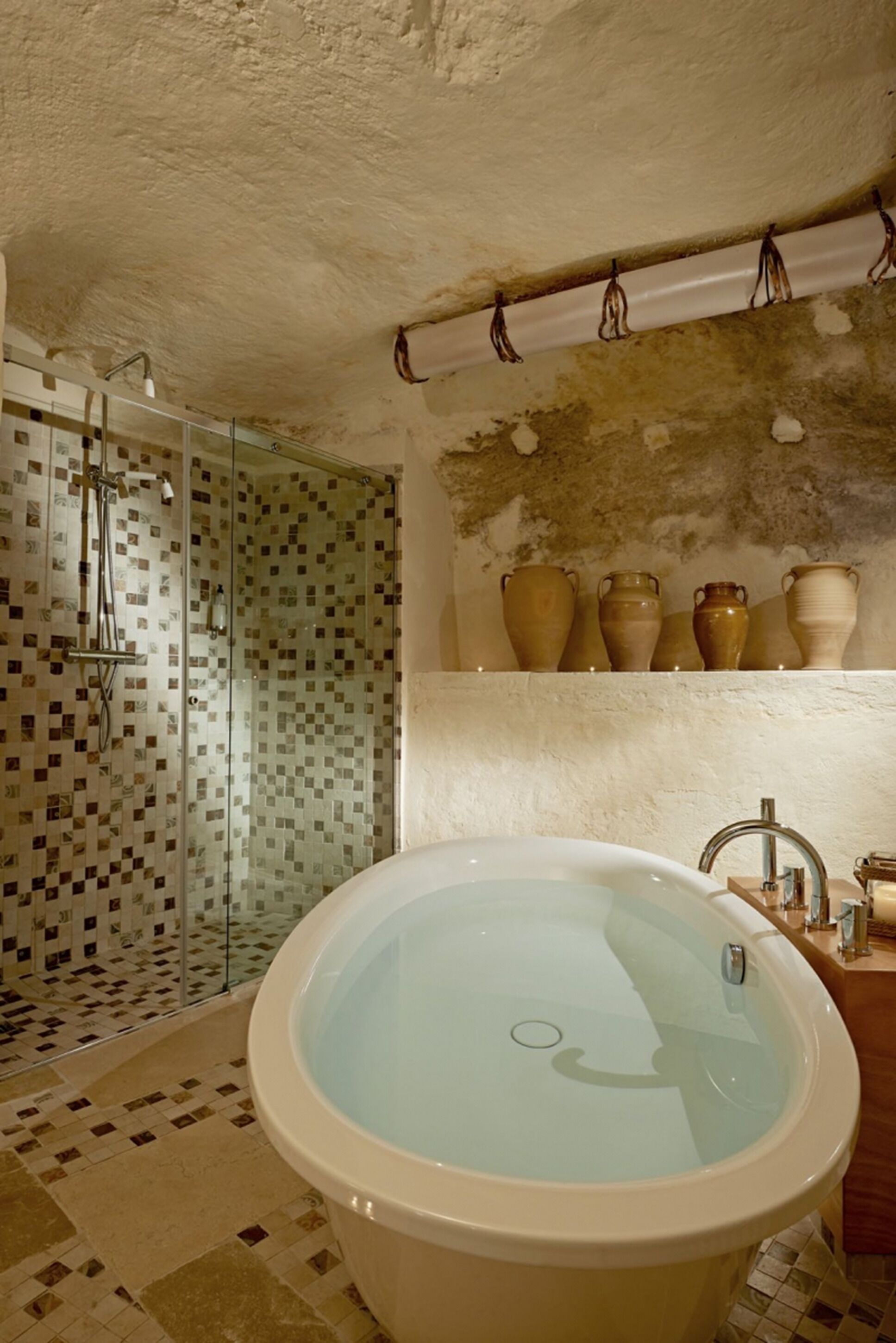 A bathroom with a glass-enclosed shower, a freestanding bathtub, and a shelf with ceramic vases.