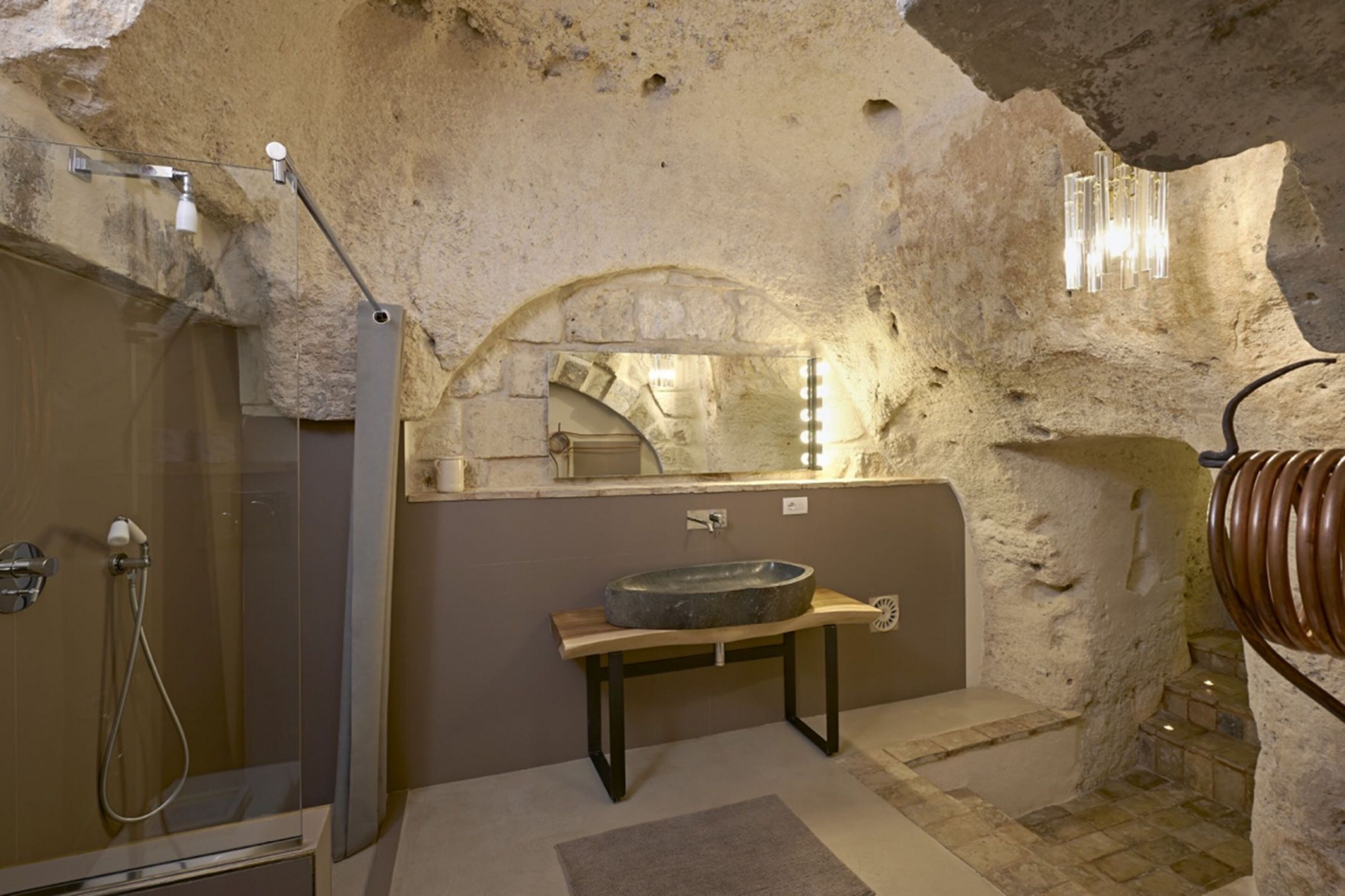 A bathroom with a stone sink, shower, and a mirror.