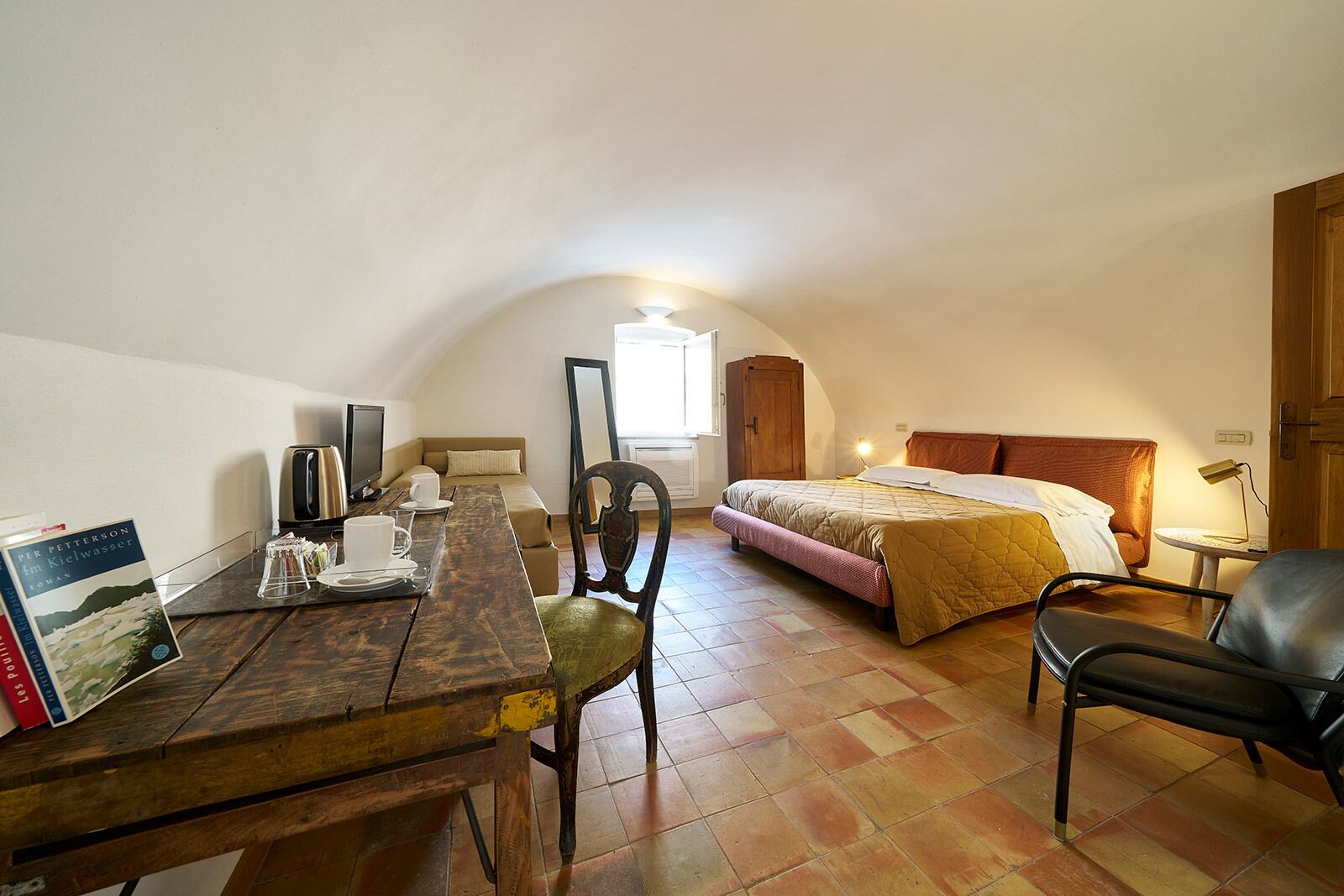Una habitación acogedora con una mesa de madera, una cama, una silla y una mesita de noche con una lámpara.