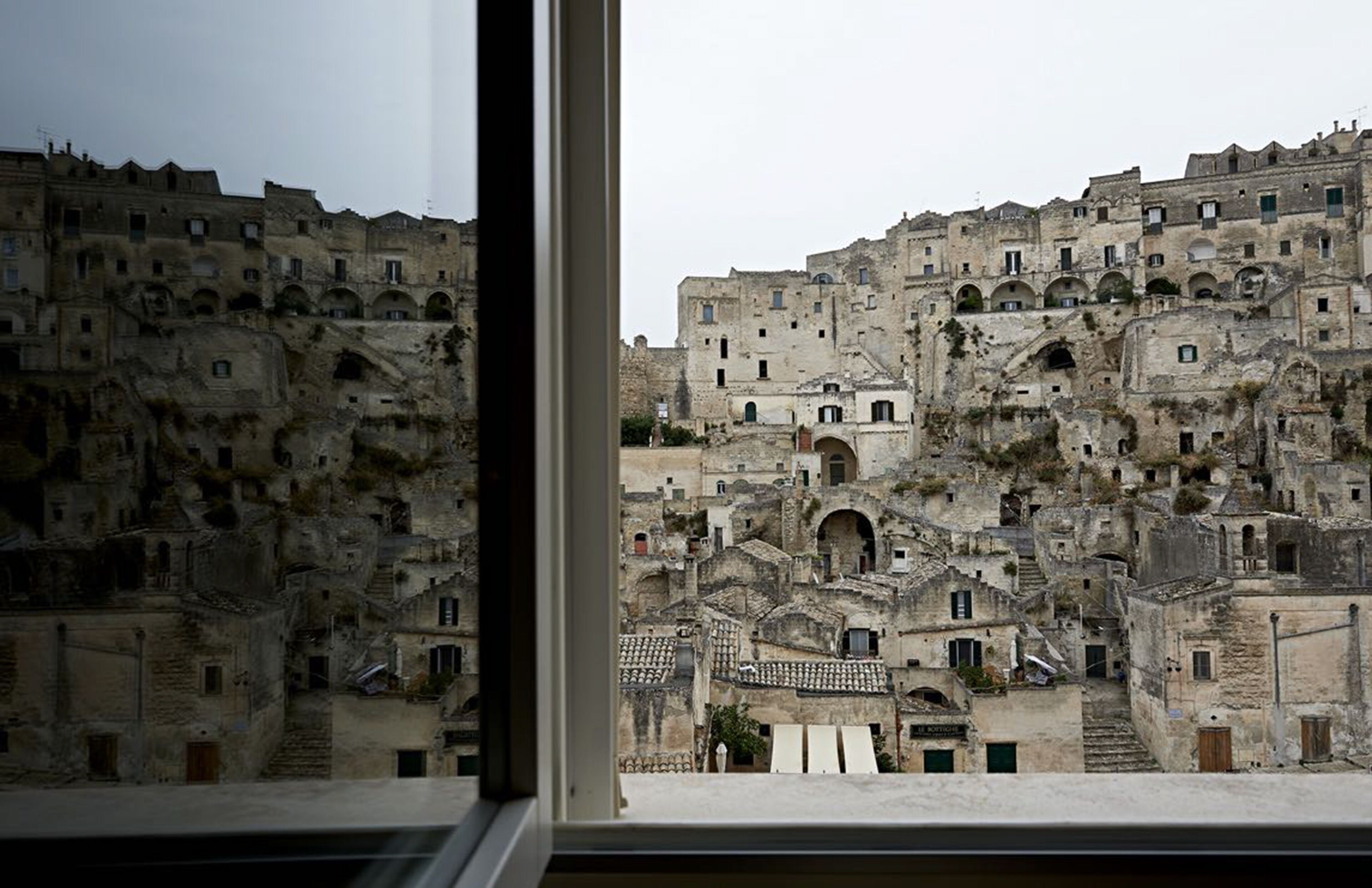 Un edificio de piedra histórico con varios niveles y puertas arqueadas, visto desde una ventana.