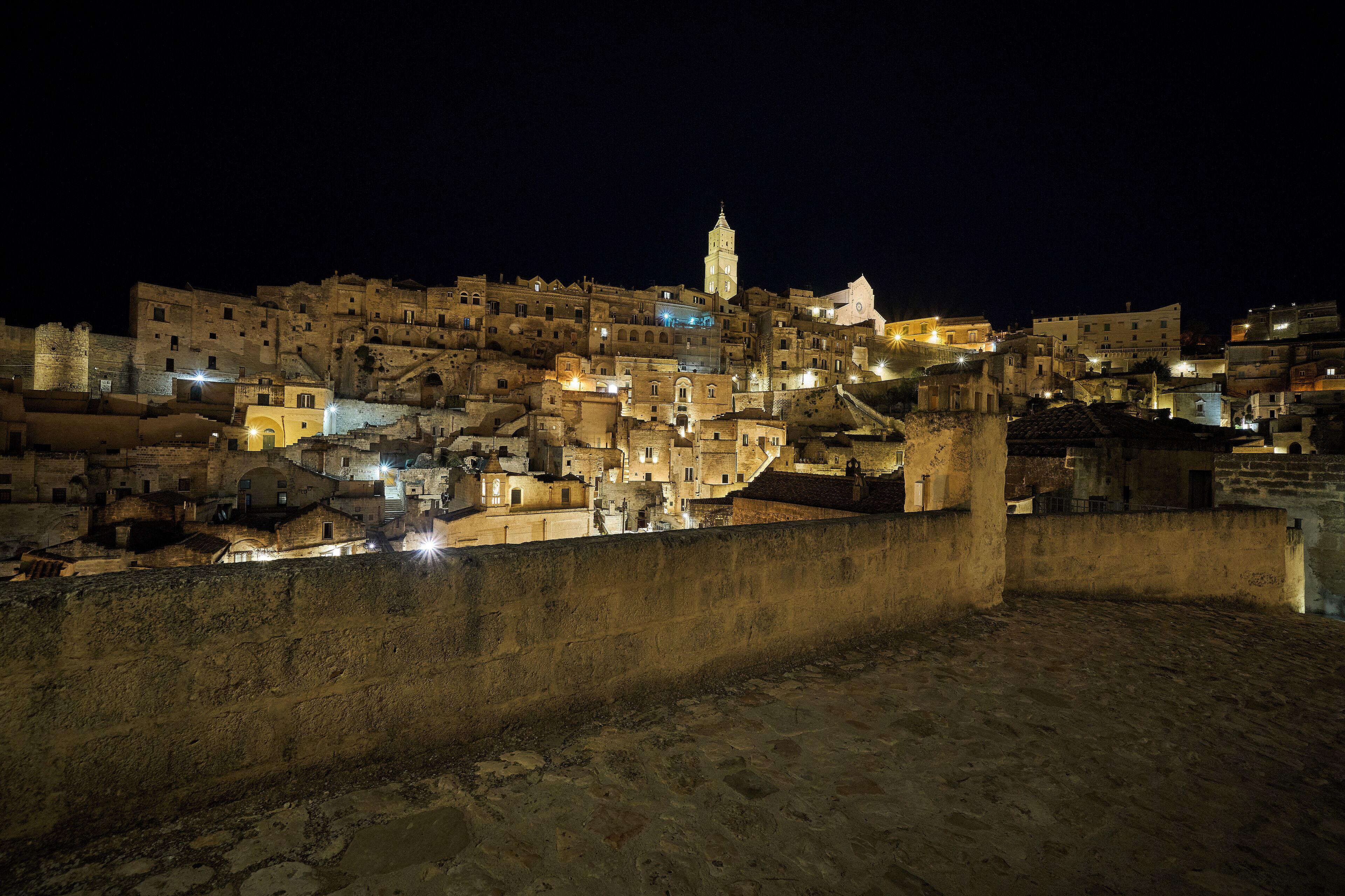 Un poble històric de nit amb edificis il·luminats i una torre destacada.