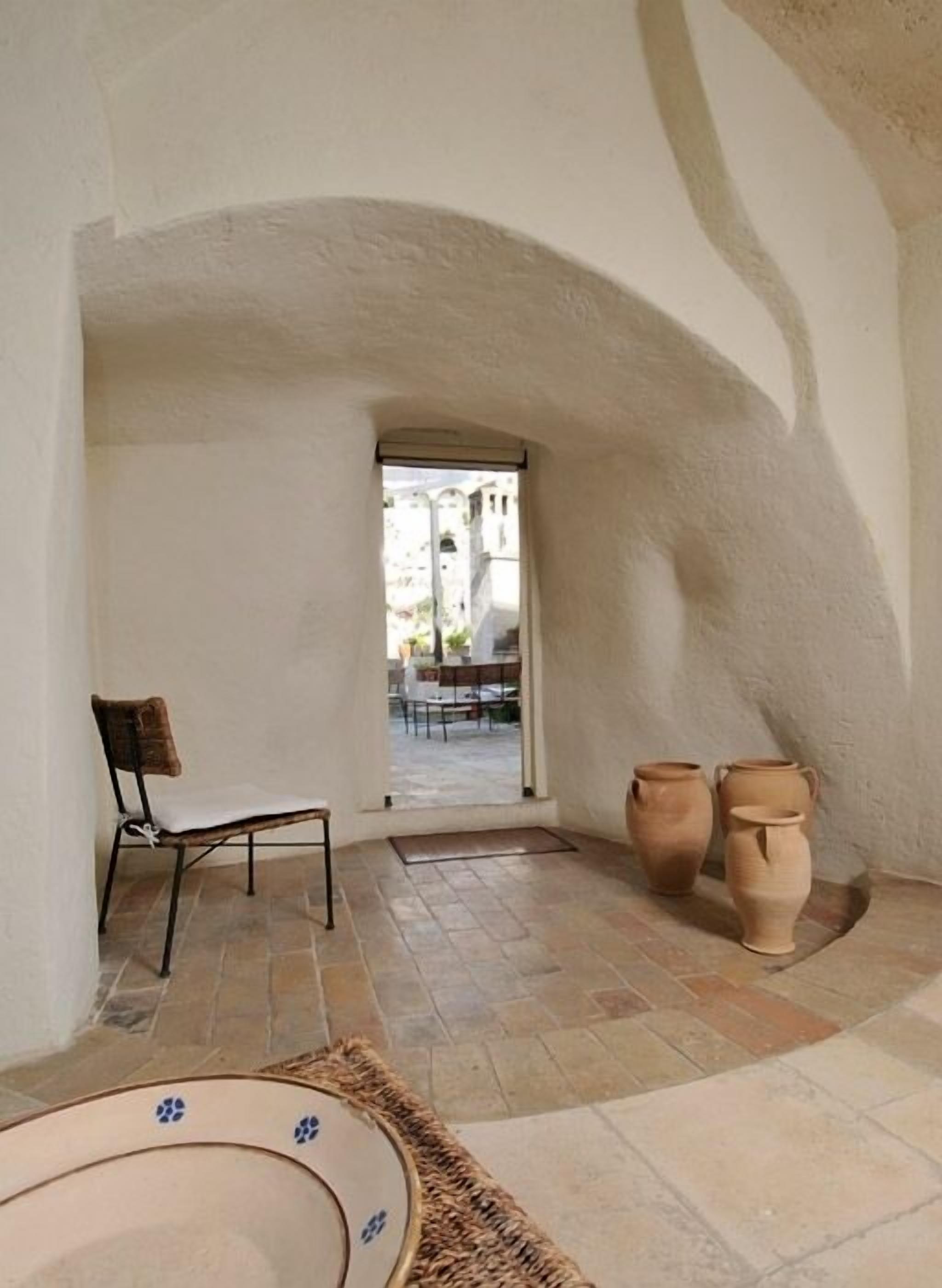 A room with a chair, a small table, and two large vases on the floor.