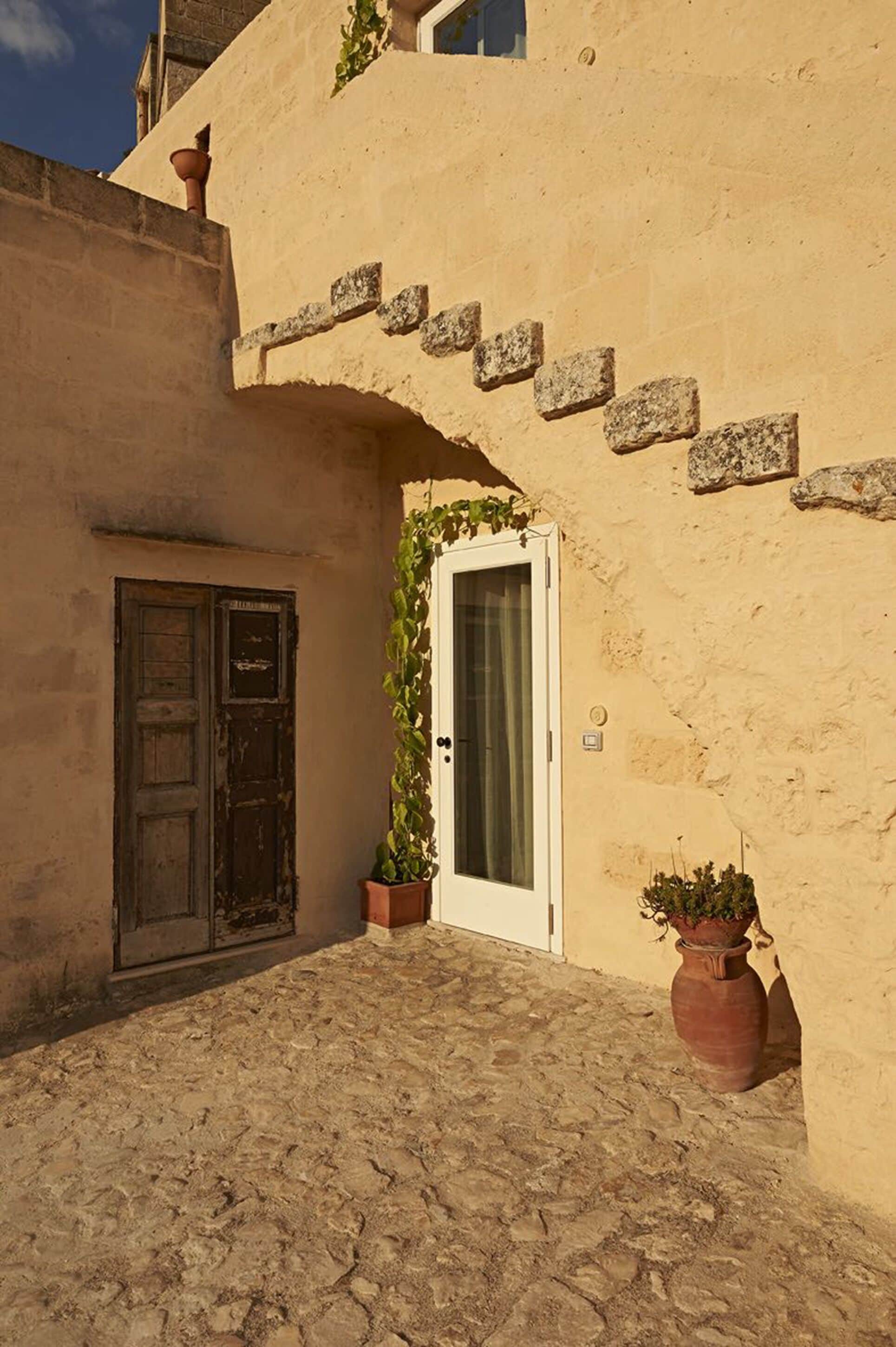 A narrow cobblestone courtyard with a rustic door and a white-framed window.