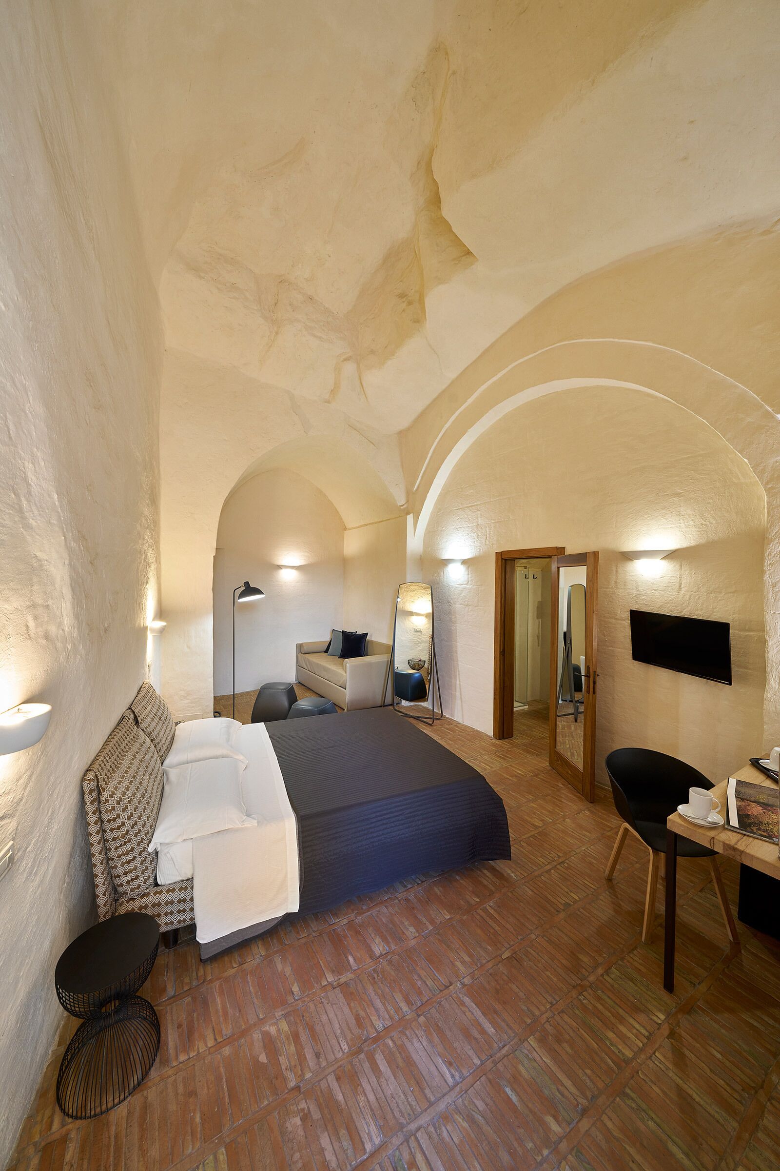 A bedroom with a large bed, a desk, a chair, a mirror, and a TV.