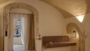 A cozy room with a stone archway, a sofa, a small table with a bottle and candle, and a view through the archway. - Fra i Sassi - Residence (Matera)