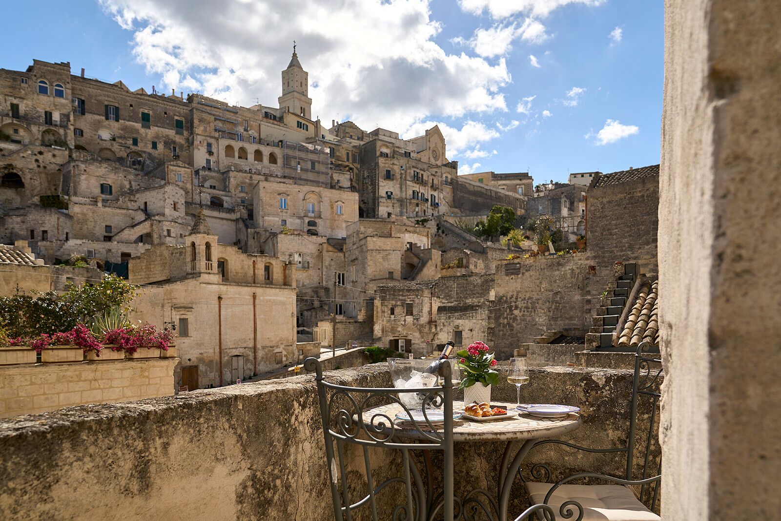 A terrace with a table set for dining, overlooking a historic cityscape with old buildings and a prominent tower.