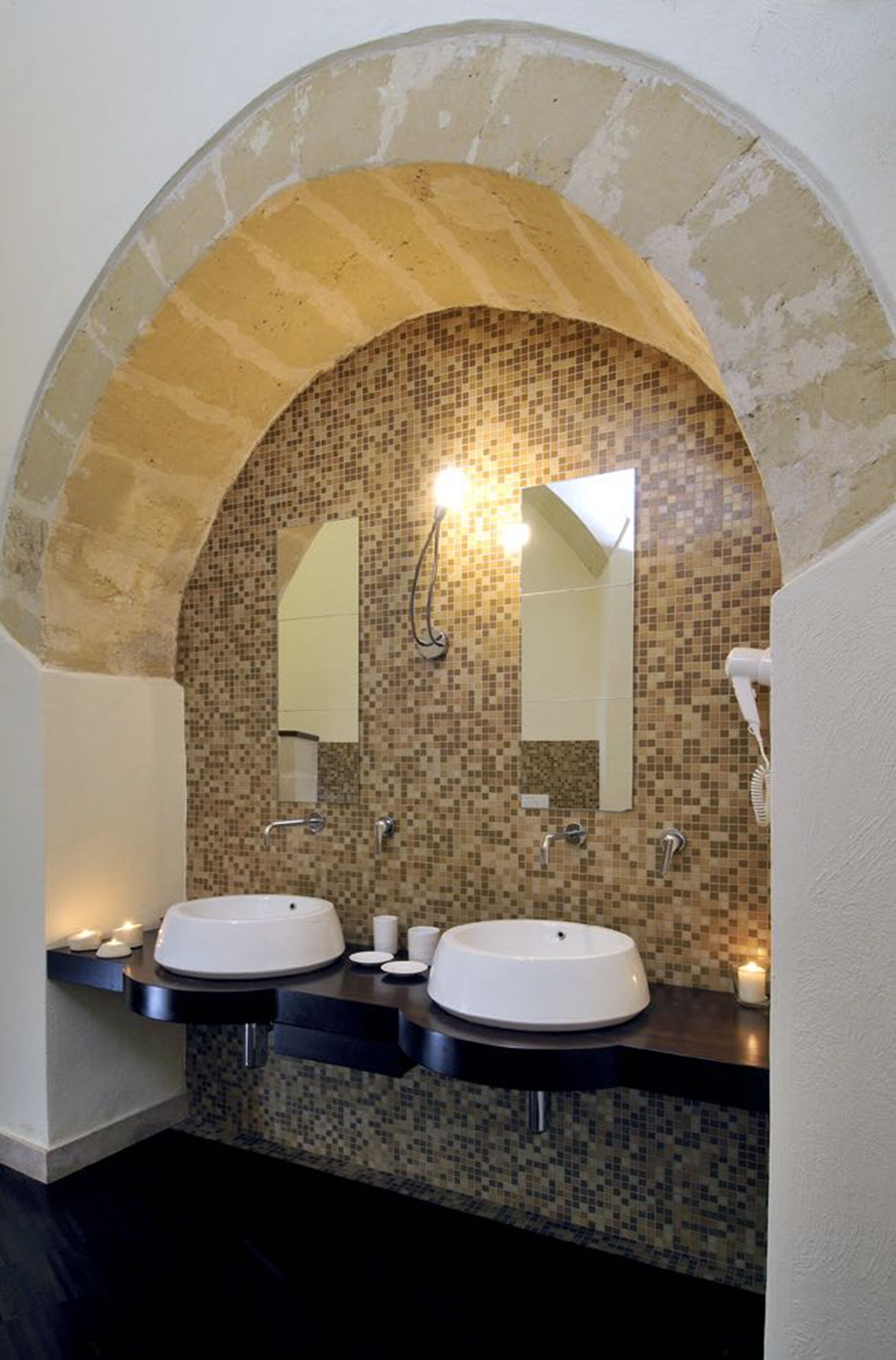 Un baño con dos lavamanos, un salpicadero de azulejos y un arco de piedra.