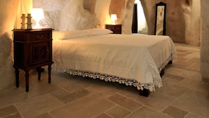 A bedroom with a stone archway, a bed with a lace bedspread, two bedside tables with lamps, and a mirror on the wall. - Fra i Sassi - Residence (Matera)