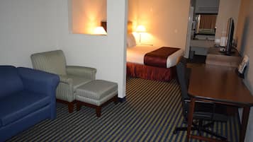 Habitación de hotel con un sofá azul, un sillón pequeño, una cama con colcha roja, un escritorio con computadora y un espejo.