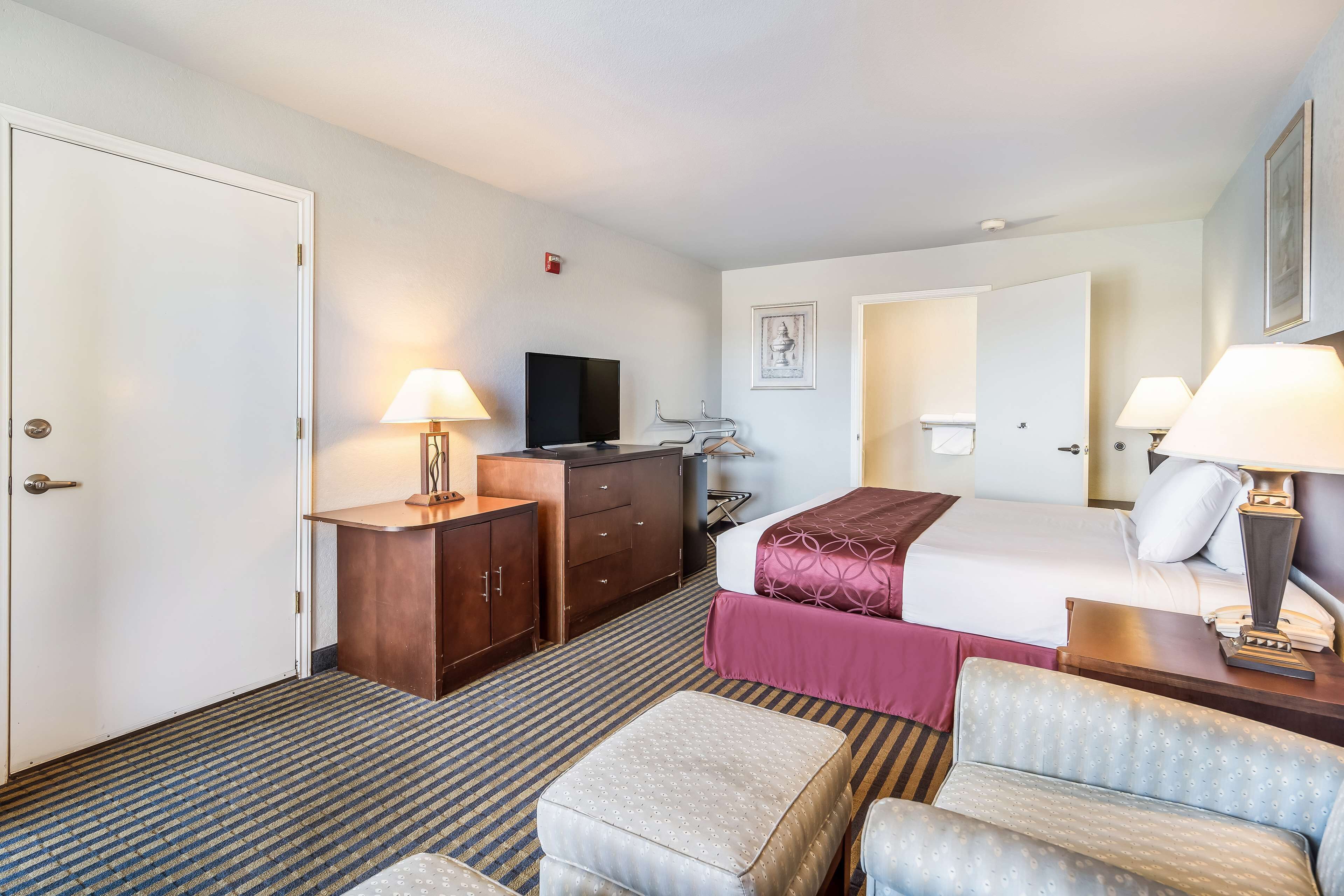 A hotel room with a bed, a desk, a television, a dresser, and a seating area with a chair and ottoman.