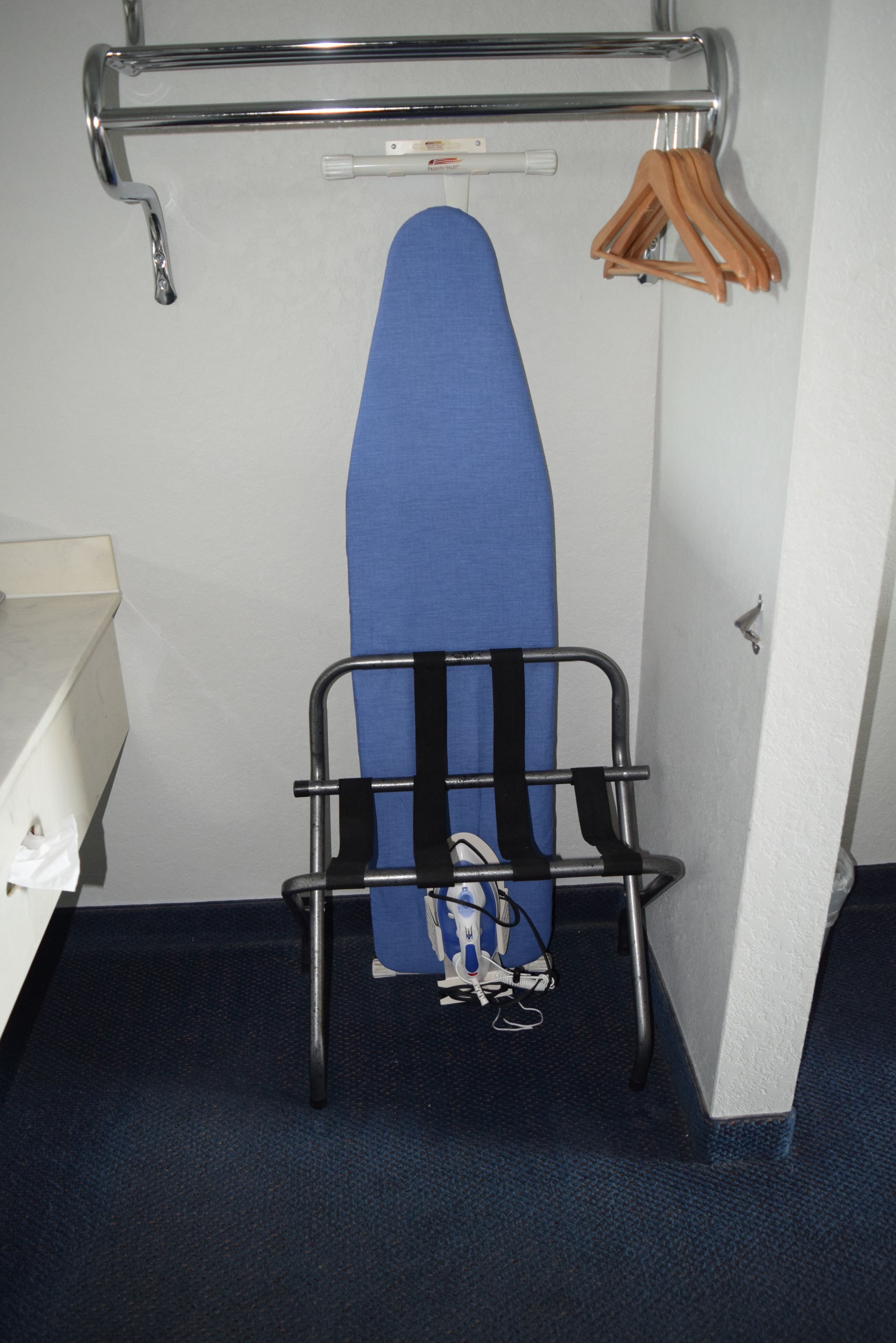 A room with a blue ironing board, a metal rack, and a white sink.