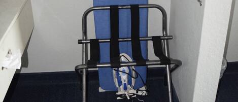 A room with a blue ironing board, a metal rack, and a white sink.