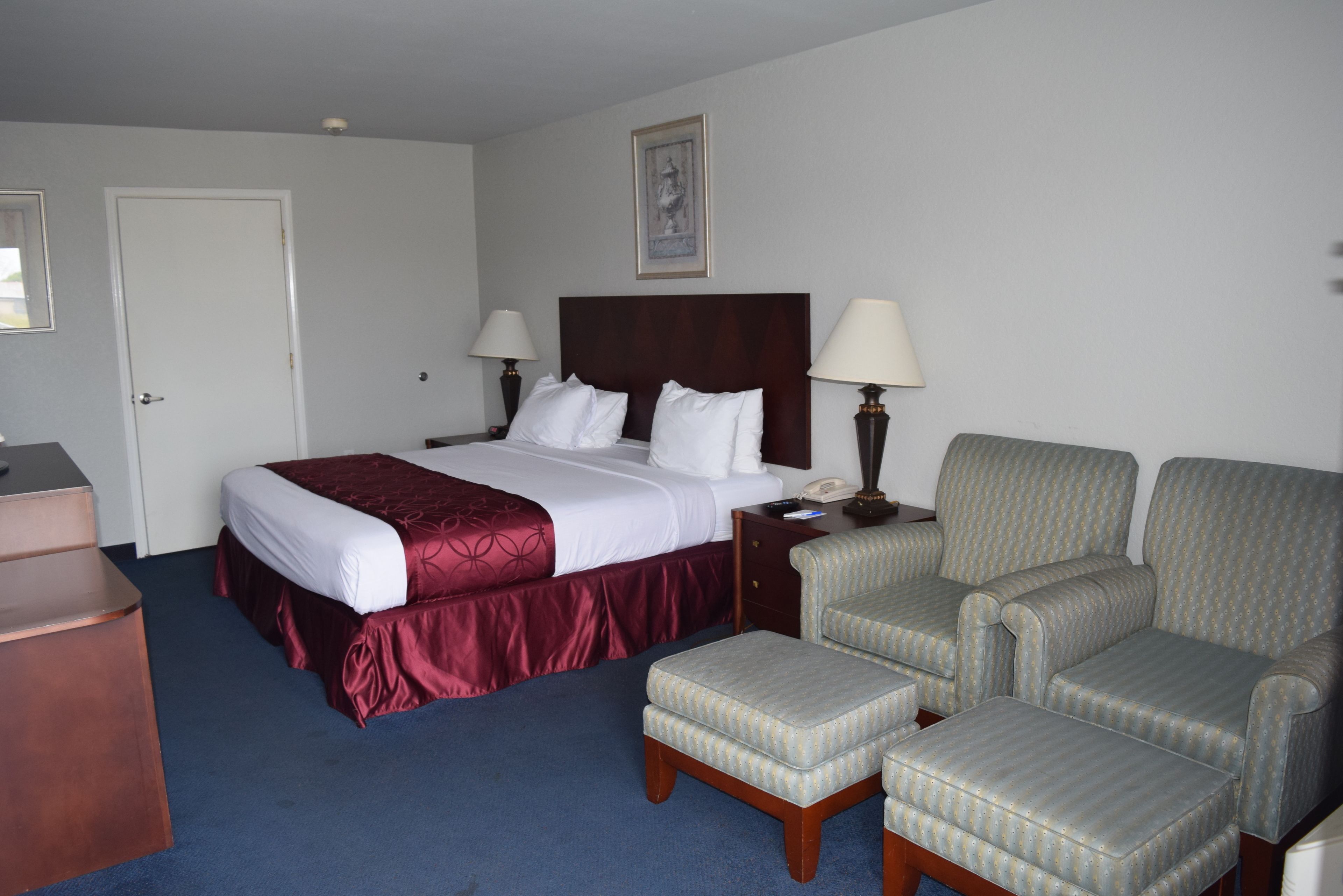 Quarto de hotel com uma cama, duas luminárias de cabeceira, uma escrivaninha, uma cadeira e um banquinho.