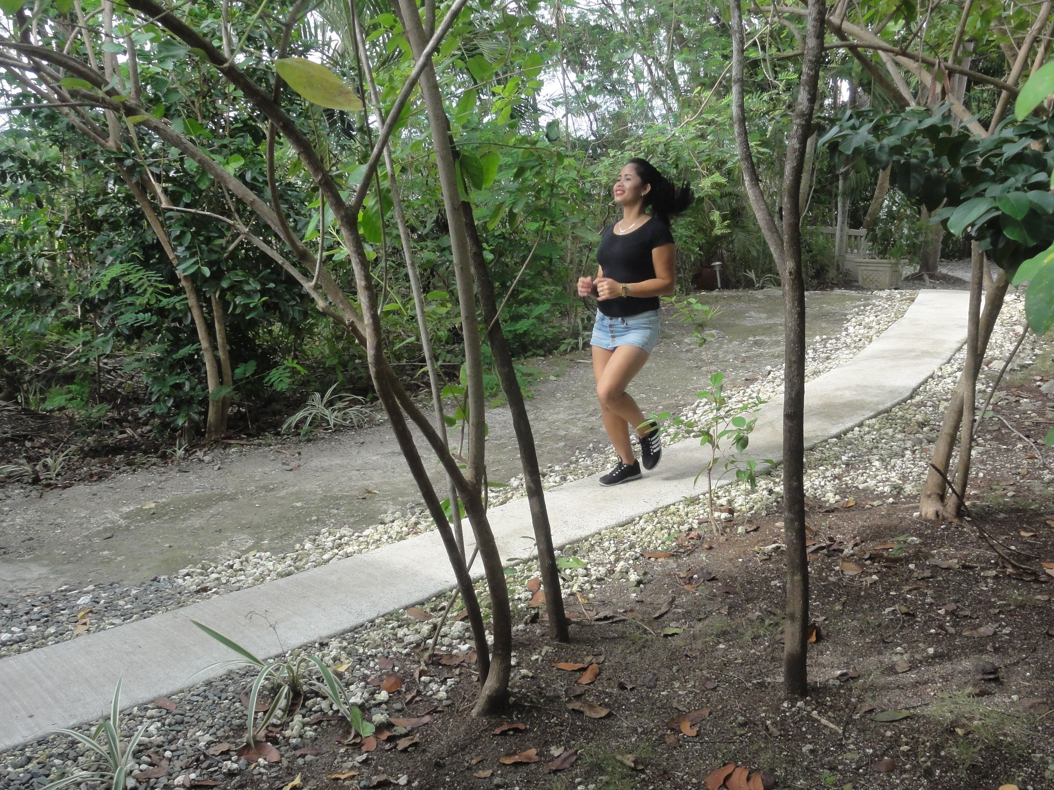 Una mujer caminando por un sendero de concreto bordeado de árboles y follaje.