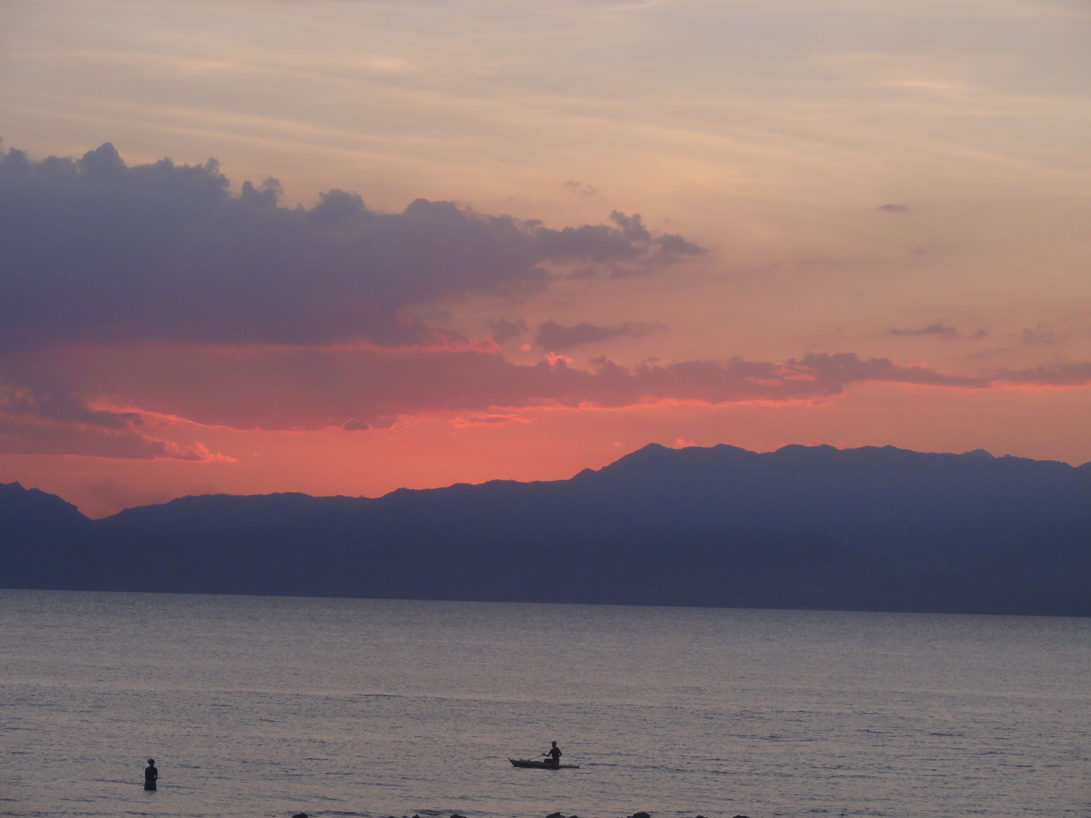 A calm lake with mountains in the background and a sunset sky.