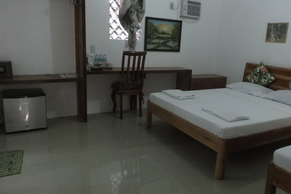 A bedroom with a bed, a desk, a chair, and a small trash bin.