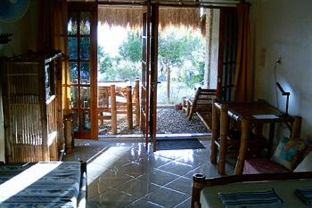 A room with a sliding glass door leading to an outdoor area, a wooden table, a sofa, and a fan on the wall.